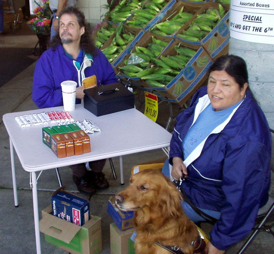 Terry and Viola, with her dog guide Alberta, at a table selling candy